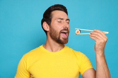 Photo of Handsome man eating sushi roll with chopsticks on light blue background