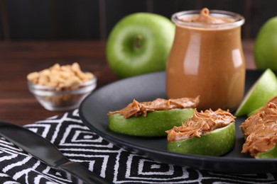 Photo of Slices of fresh green apple with peanut butter on wooden table, closeup