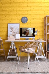 Stylish home office interior with comfortable workplace near yellow brick wall