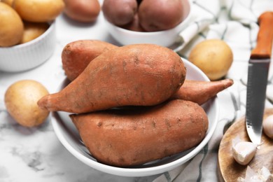 Photo of Different types of fresh potatoes in bowls on white marble table, closeup