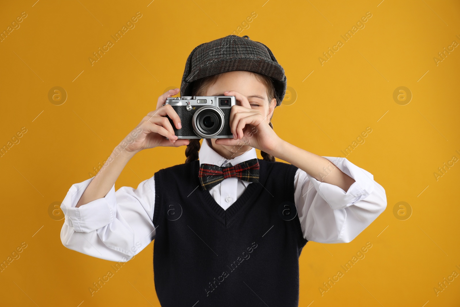 Photo of Cute little detective taking photo with vintage camera on yellow background