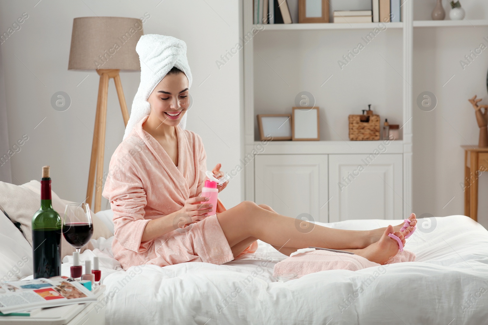 Photo of Beautiful young woman preparing toenails for pedicure on bed at home