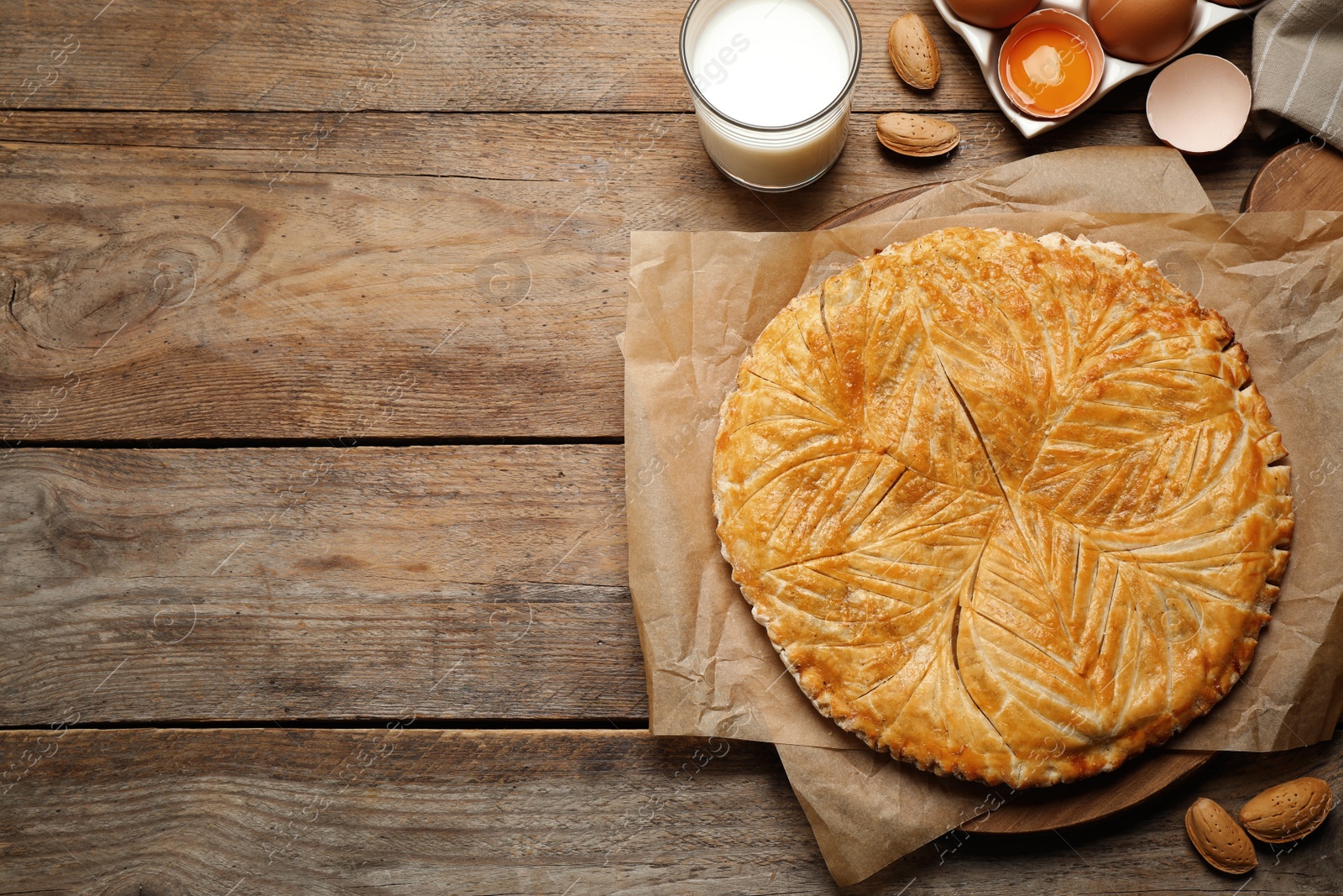 Photo of Traditional galette des rois and ingredients on wooden table, flat lay. Space for text