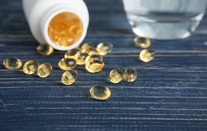 Photo of Cod liver oil pills and glass of water on table, closeup