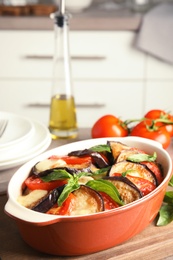 Photo of Baked eggplant with tomatoes, cheese and basil in dishware on table