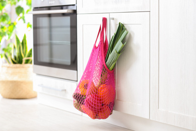 Photo of Net bag with vegetables hanging on cabinet door in kitchen