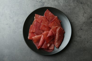 Photo of Plate with tasty bresaola on grey table, top view