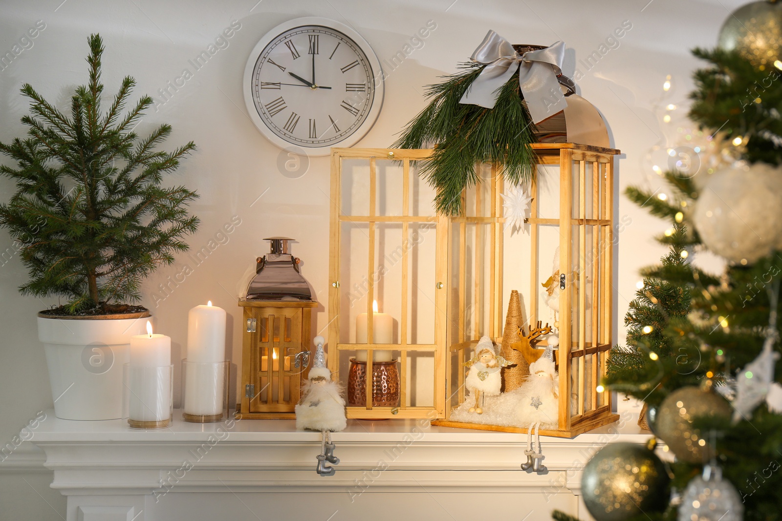 Photo of Beautiful wooden lanterns and other decorations on mantelpiece in room with Christmas tree