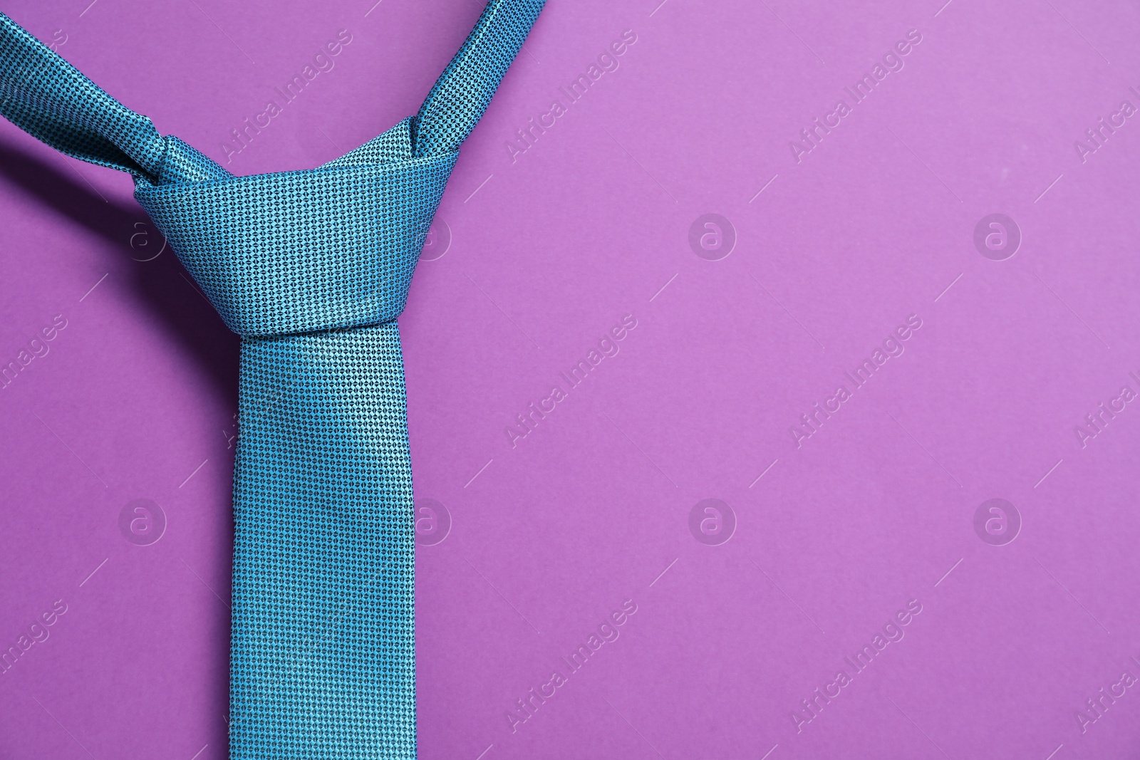 Photo of Turquoise necktie on purple background, top view. Space for text