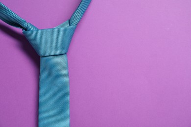 Turquoise necktie on purple background, top view. Space for text