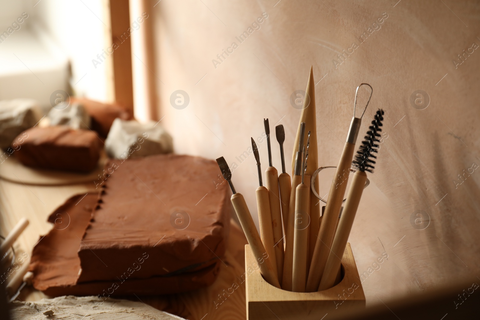 Photo of Clay and set of modeling tools on table in workshop, closeup