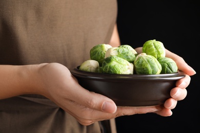 Photo of Woman holding bowl with Brussels sprouts on black background, closeup