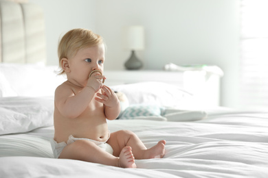 Cute little baby in diaper with pacifier sitting on bed at home. Space for text