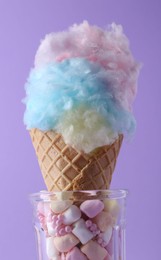 Photo of Sweet cotton candy in waffle cone on purple background, closeup