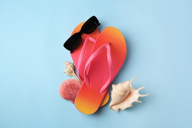 Sunglasses, flip flops and shells on light blue background, flat lay. Beach accessories