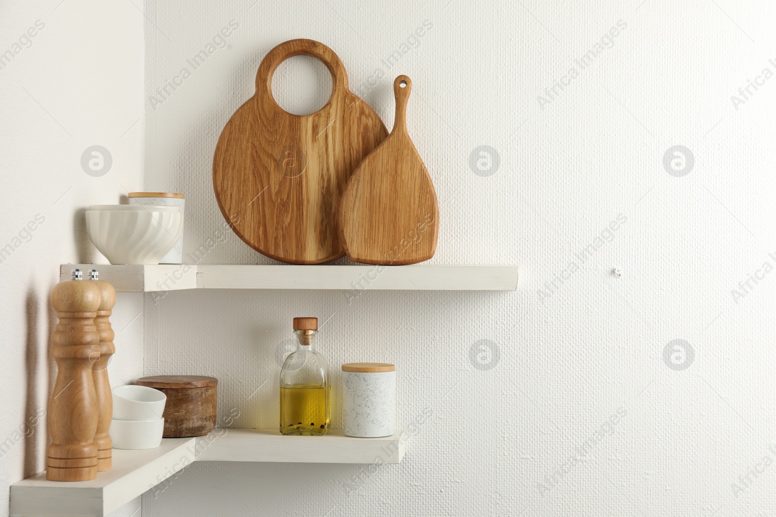 Photo of Wooden cutting boards, dishware and kitchen utensils on white shelves, space for text