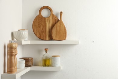 Wooden cutting boards, dishware and kitchen utensils on white shelves, space for text