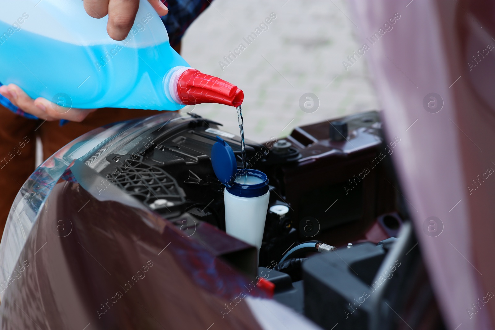 Photo of Man pouring liquid from plastic canister into car washer fluid reservoir, closeup