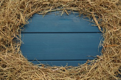 Frame of dried hay on blue wooden background, flat lay. Space for text