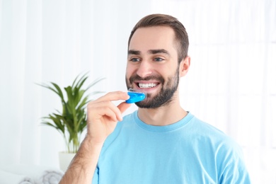 Young man using teeth whitening device at home