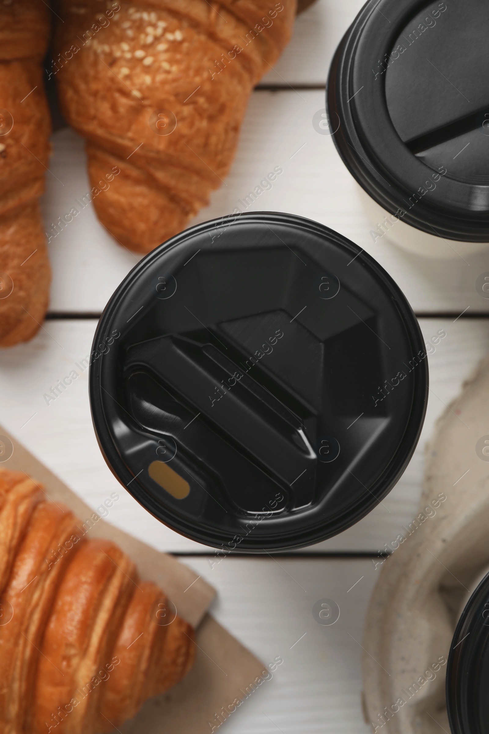 Photo of Coffee to go. Paper cups with tasty drink and croissants on white wooden table, flat lay