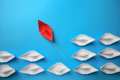 Photo of Red paper boat floating away from others on light blue background, flat lay. Uniqueness concept