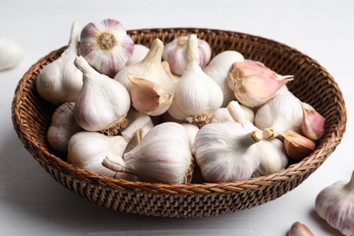 Fresh organic garlic in wicker basket on white table, closeup