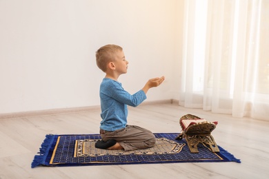 Little Muslim boy with Koran praying on rug indoors