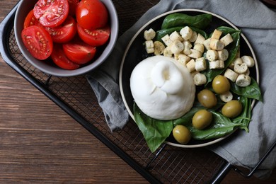 Photo of Delicious burrata cheese served with olives, croutons, basil and tomatoes on wooden table, top view