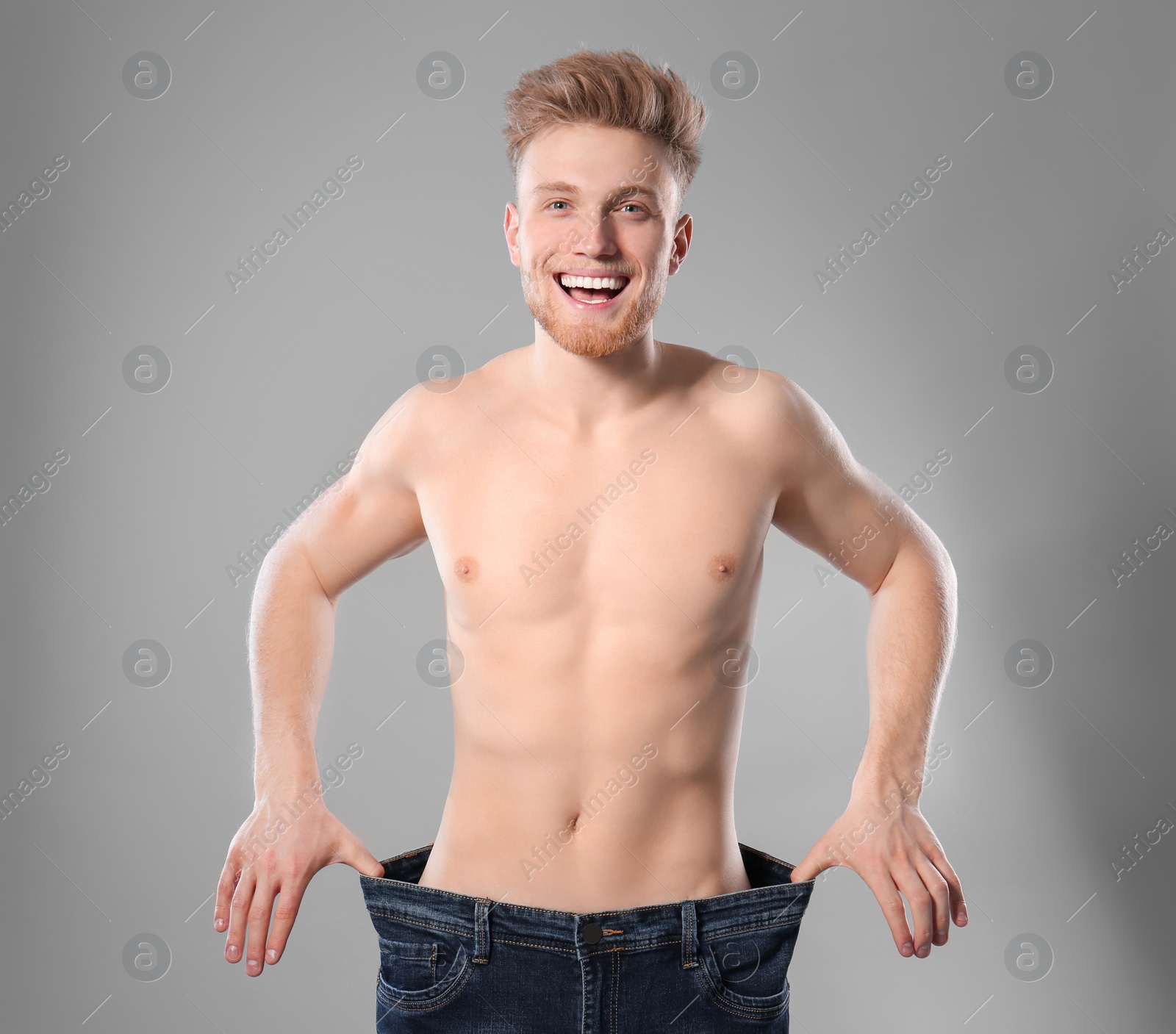 Photo of Young man with slim body in old big size jeans on grey background