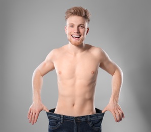 Young man with slim body in old big size jeans on grey background