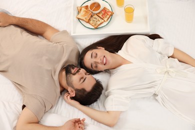 Photo of Happy couple lying on bed near white tray with breakfast, above view