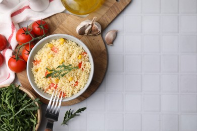 Photo of Tasty couscous with pepper, corn and arugula served on white tiled table, flat lay. Space for text