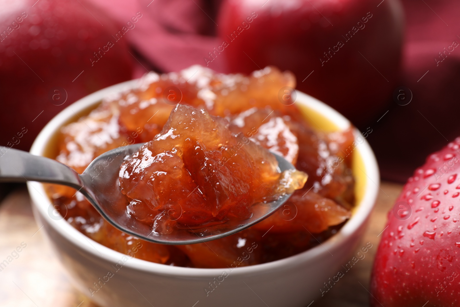 Photo of Spoon with delicious apple jam above bowl on table, closeup