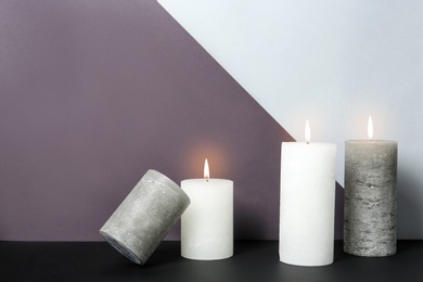 Photo of Different decorative wax candles on table against color background