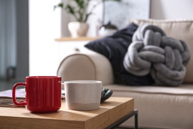 Wooden table with cups near comfortable sofa in living room interior. Space for text