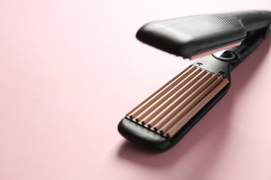 Photo of Modern corrugated hair iron on pink background, closeup. Space for text