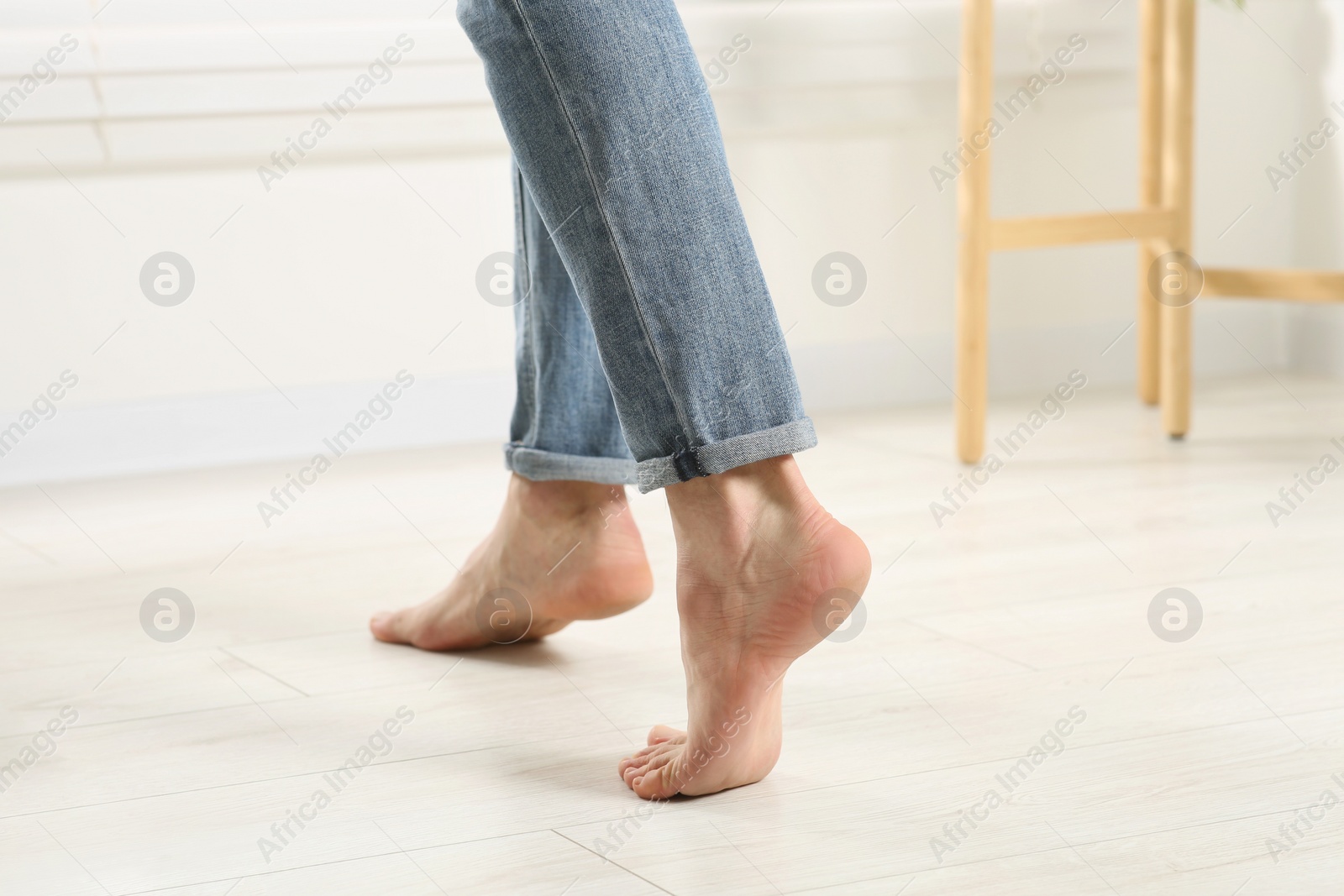 Photo of Barefoot woman walking on white parquet at home, closeup. Heated floor