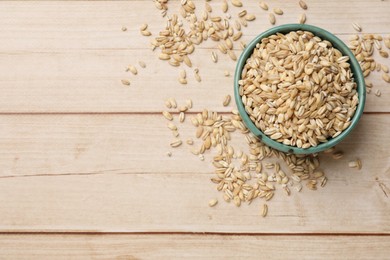 Photo of Dry pearl barley in bowl on light wooden table, top view. Space for text