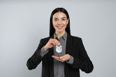 Businesswoman holding alarm clock on light grey background. Time management