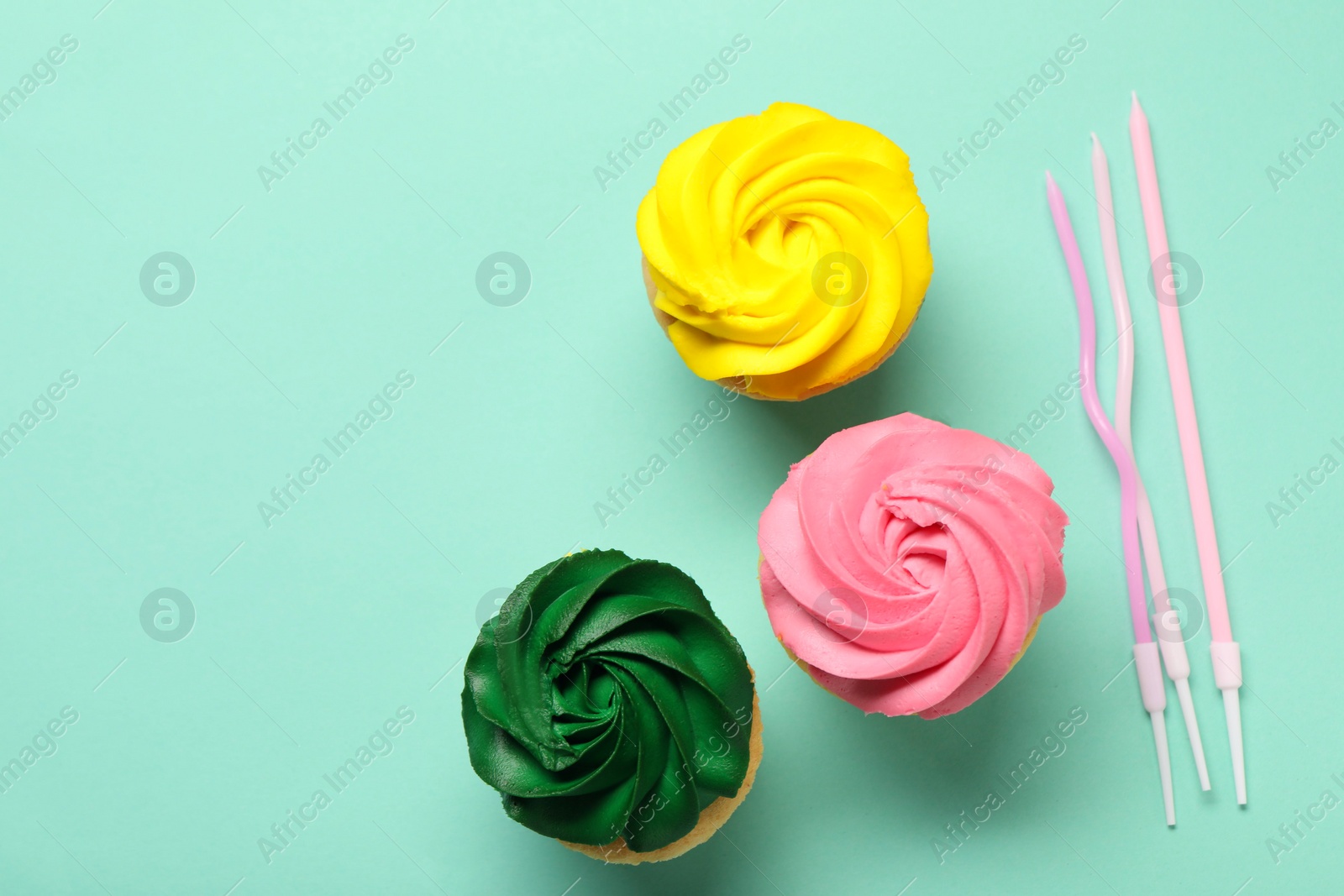 Photo of Delicious cupcakes with bright cream and candles on turquoise background, flat lay. Space for text