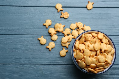 Delicious goldfish crackers in bowl on blue wooden table, flat lay