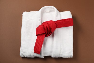 Photo of Red karate belt and white kimono on brown background, top view