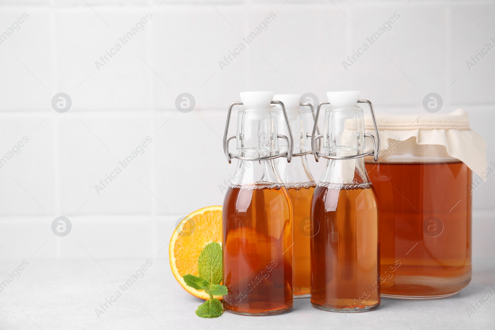 Photo of Tasty kombucha, orange and mint on white table, space for text