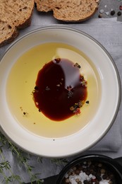 Photo of Bowl of organic balsamic vinegar with oil, spices and bread slices on grey table, flat lay