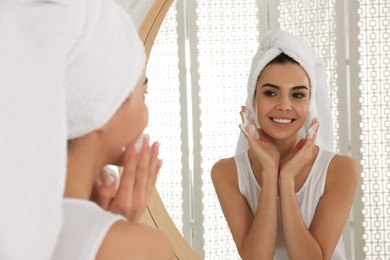 Photo of Happy young woman applying cleansing foam onto face near mirror in bathroom