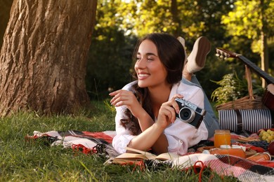 Happy young woman with camera on plaid in park. Summer picnic