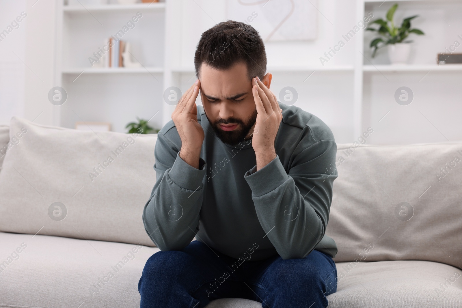 Photo of Man suffering from headache on sofa at home