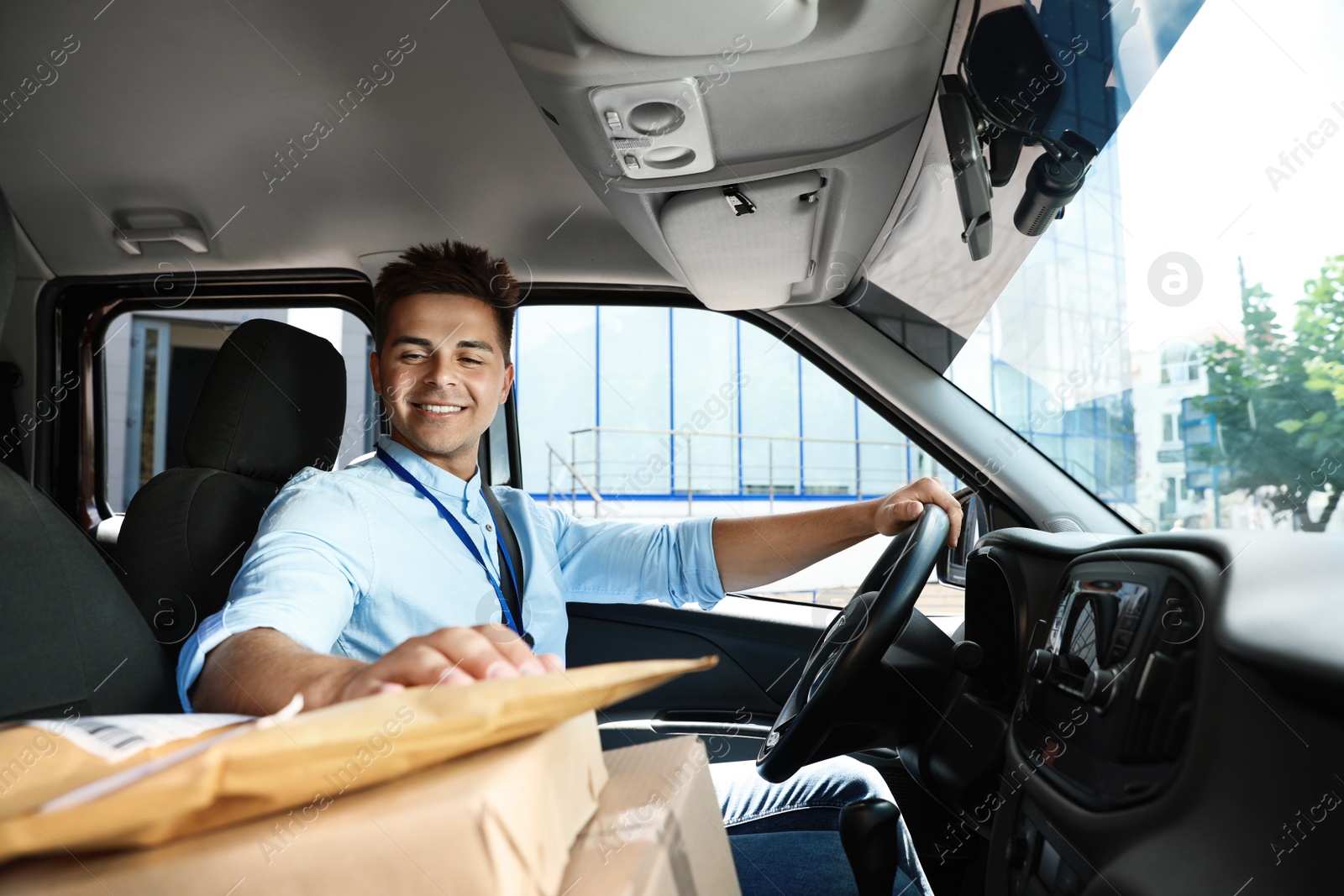 Photo of Young courier with parcels in delivery car