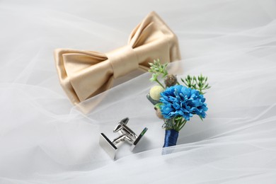 Photo of Wedding stuff. Stylish boutonniere, bow tie and cufflinks on white veil, closeup